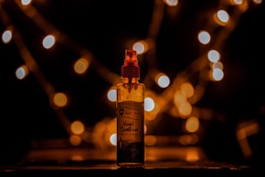 A bottle of hand sanitizer is placed on a dark surface with warm, out-of-focus lights creating a bokeh effect in the background. The lighting is soft and creates a cozy, intimate ambiance.