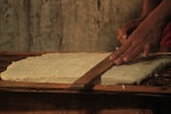 Artisan carefully carving a wooden pizza rolling board in a bright workshop.
