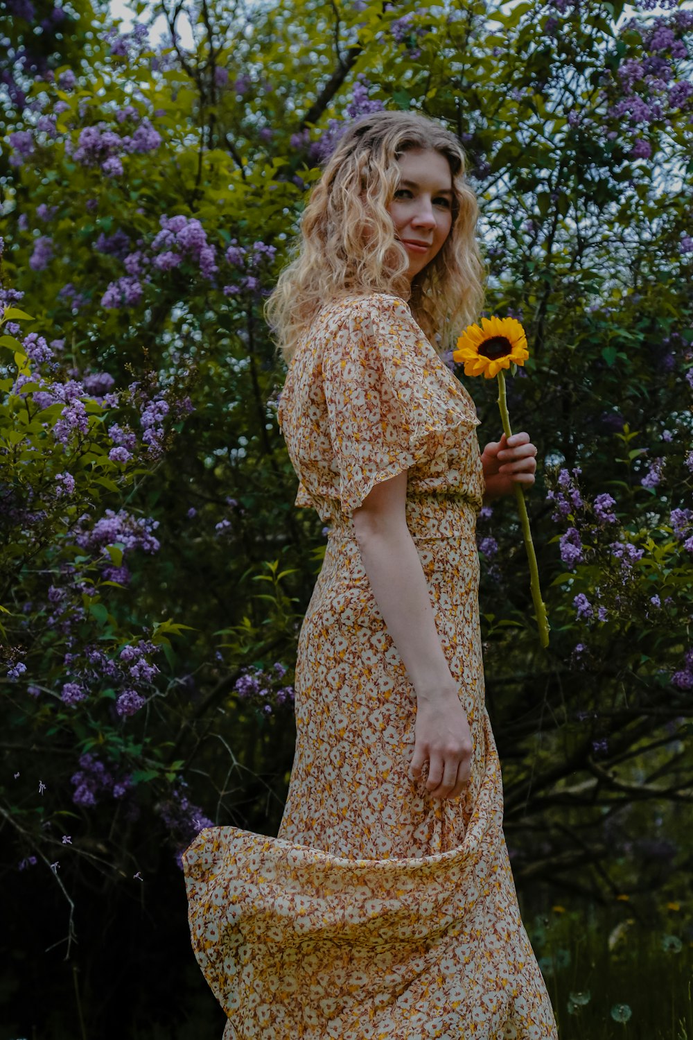 woman in yellow and white floral dress standing beside purple flowers