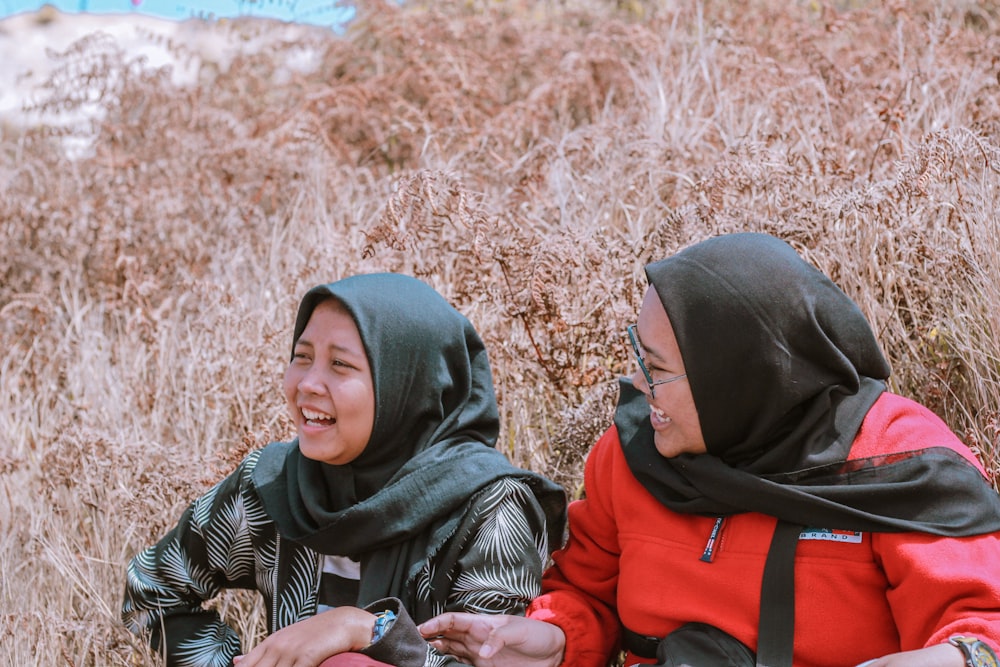 woman in black hijab and red jacket sitting on brown grass field during daytime