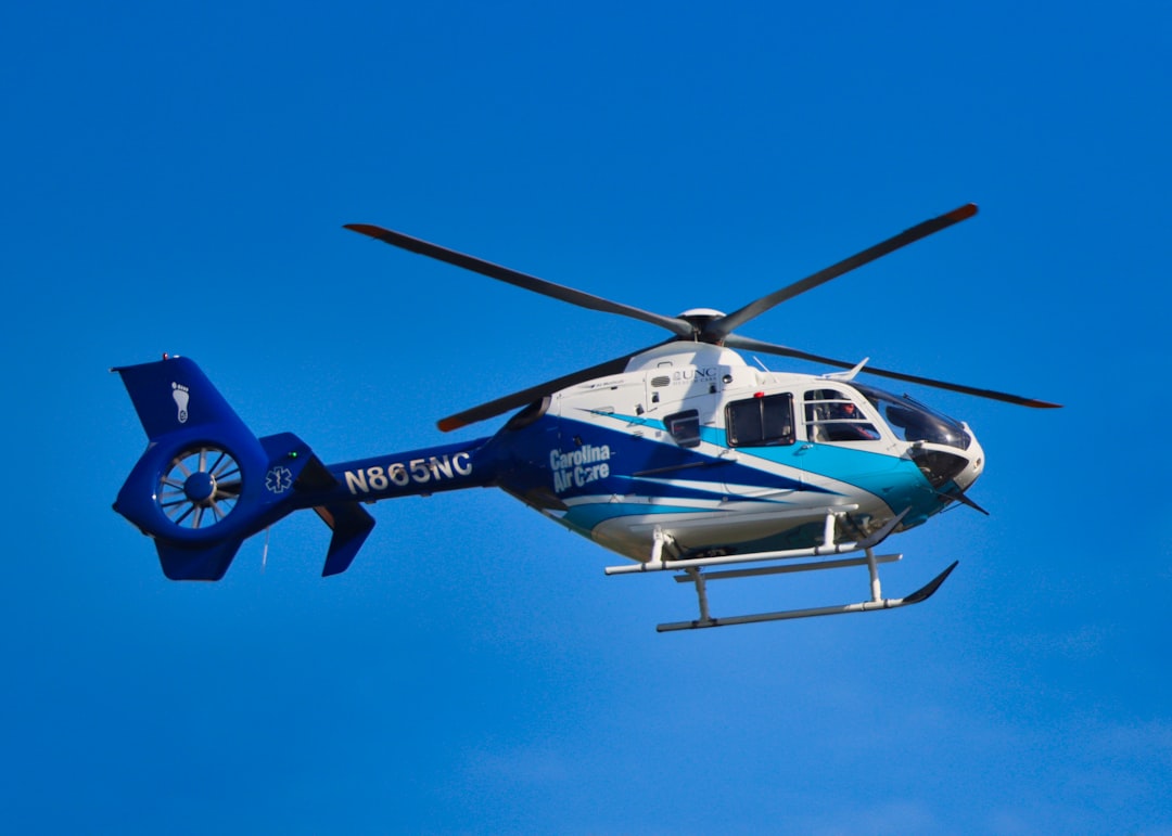 blue and white helicopter flying under blue sky during daytime