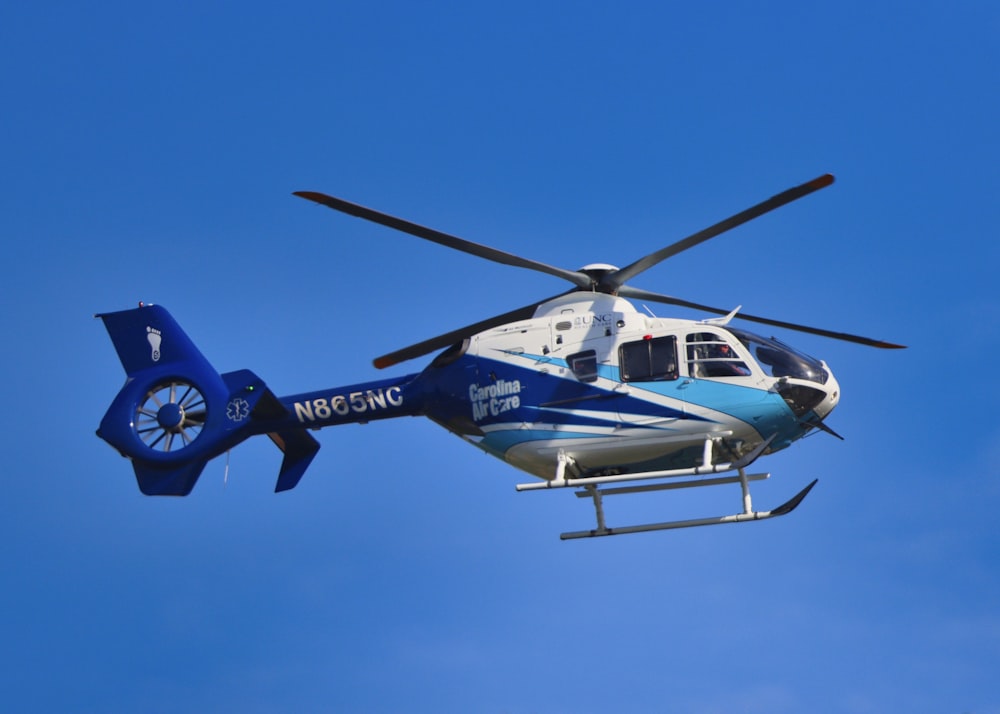 blue and white helicopter flying under blue sky during daytime