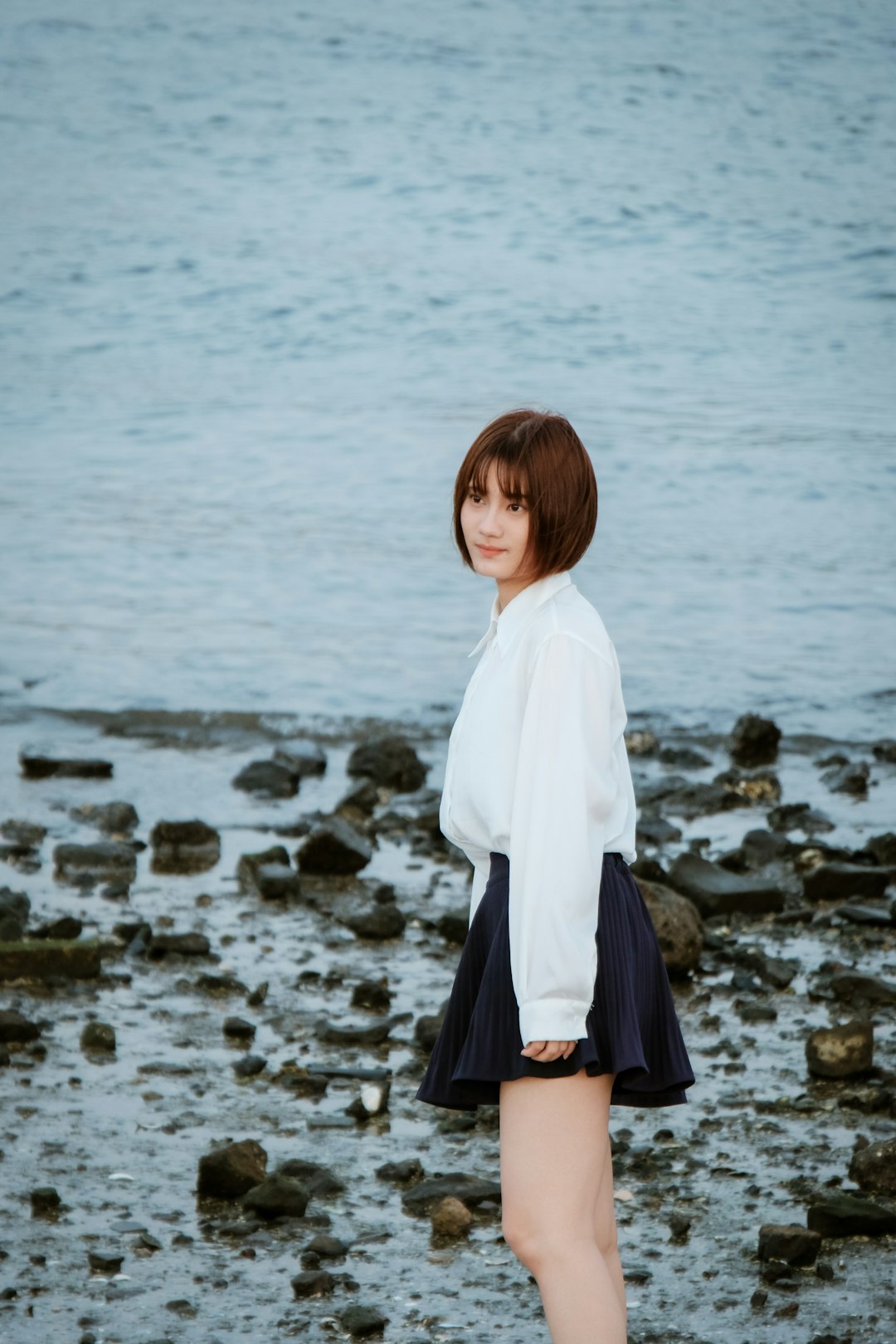 girl in white long sleeve shirt and black skirt standing on gray rock near body of on on on on