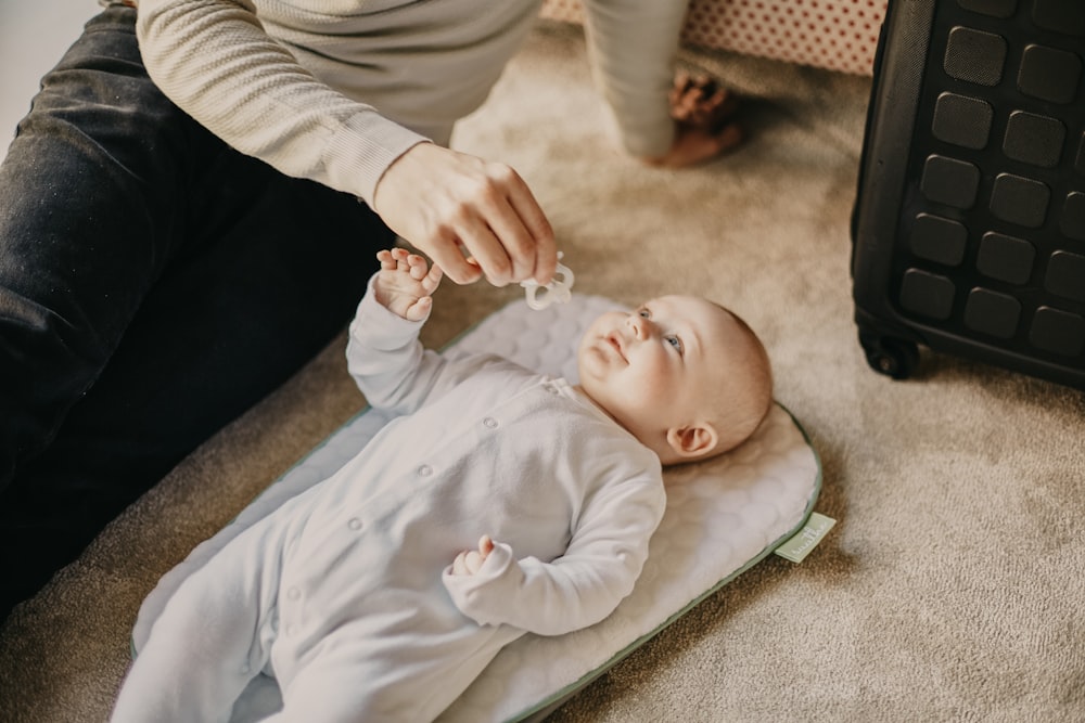 baby in white onesie lying on floor