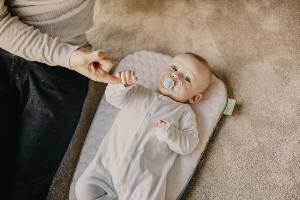 baby in white onesie lying on white textile