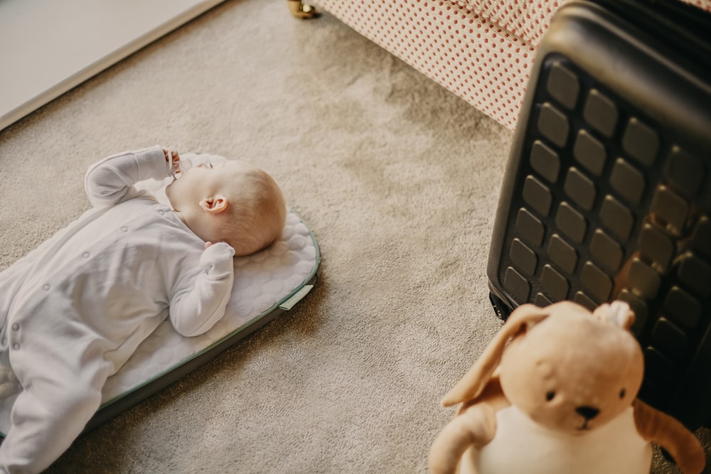 baby in white onesie lying on green and white textile