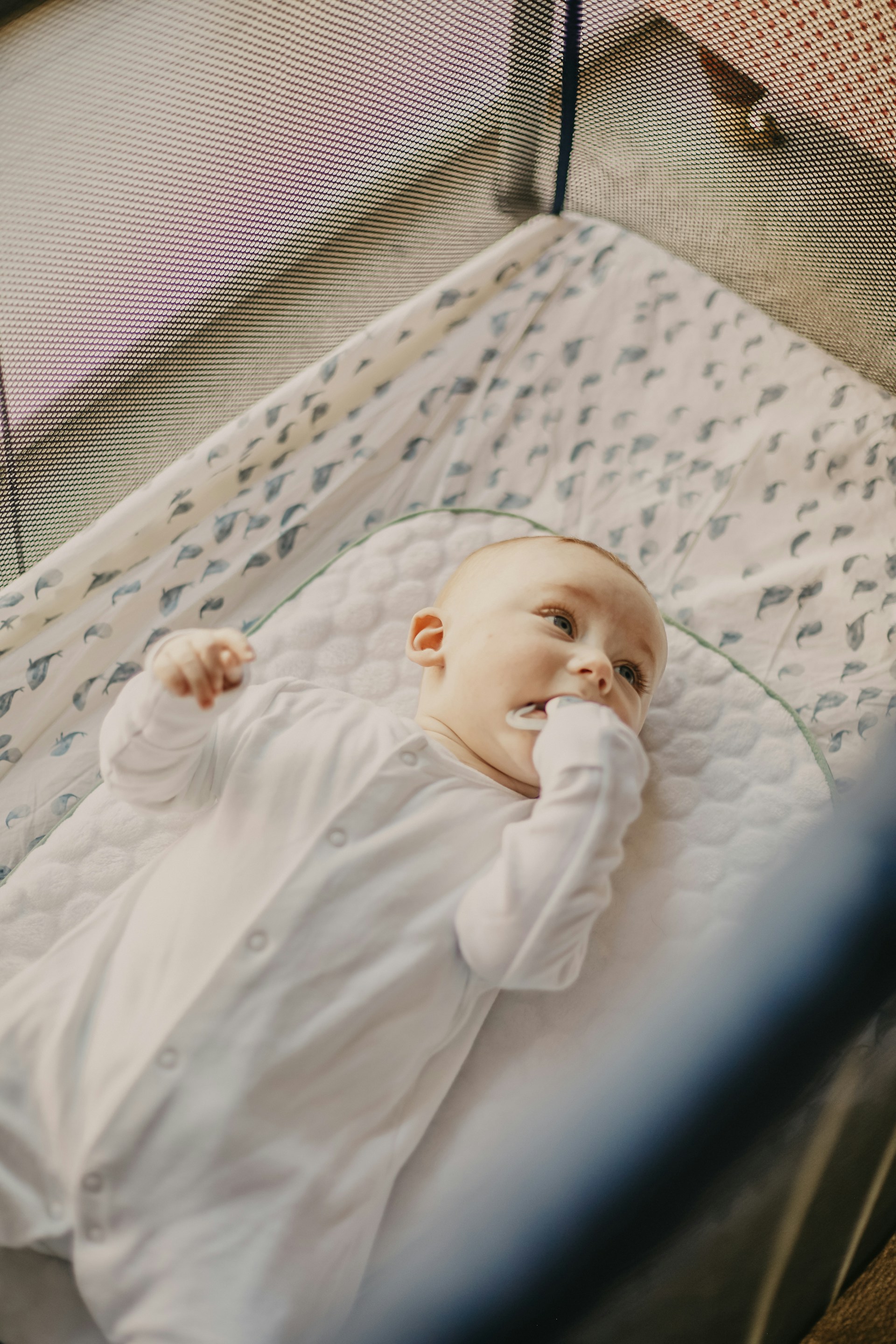 baby in white onesie lying on white and blue bed