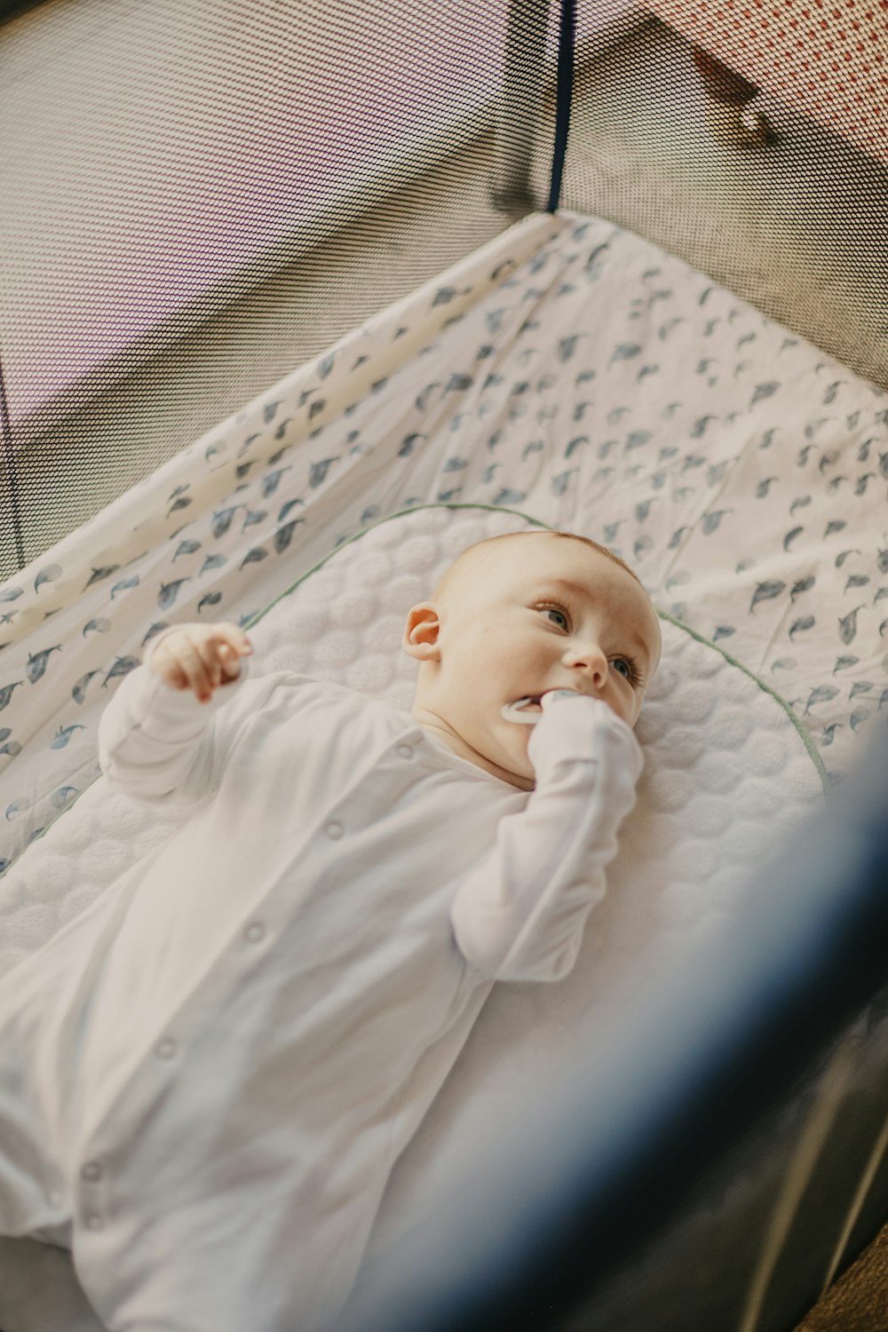 白と青のベッドに横たわる白いワンジーを着た赤ちゃん