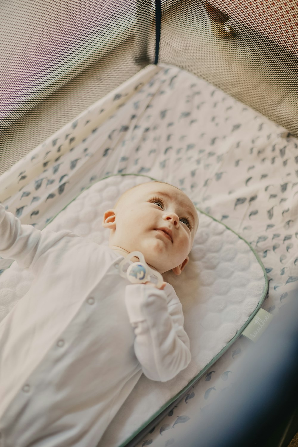 bebê no botão azul até camisa deitada na cama branca e verde