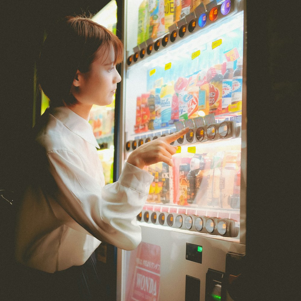 woman in white long sleeve shirt standing in front of vending machine