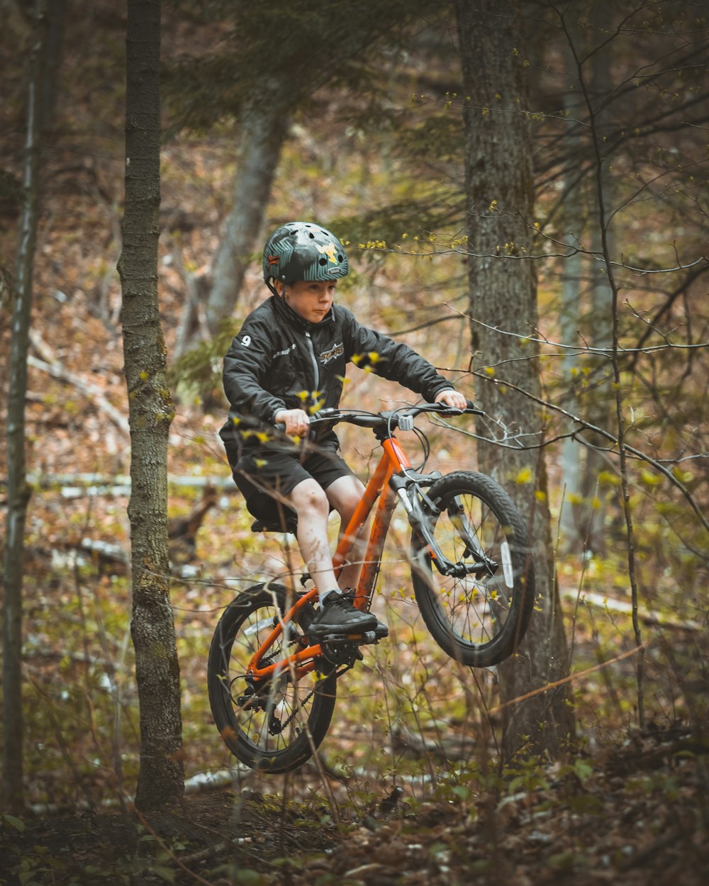 man in black jacket riding orange and black mountain bike in forest during daytime