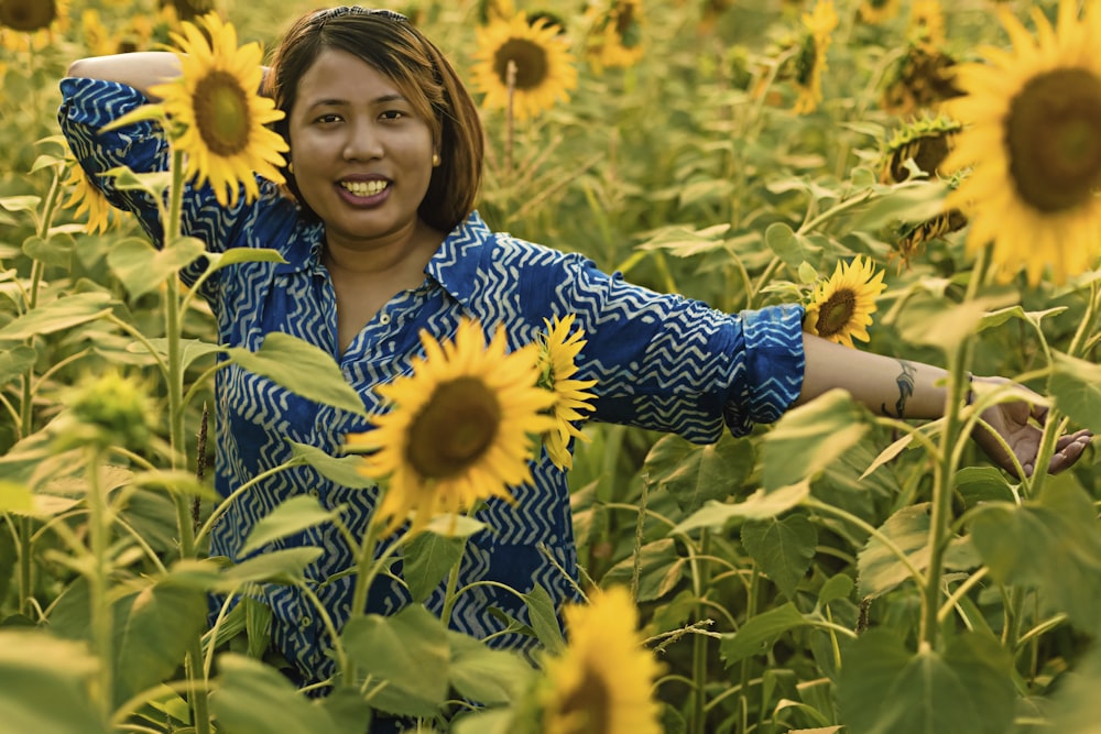 woman in blue and white floral long sleeve shirt standing on sunflower field during daytime