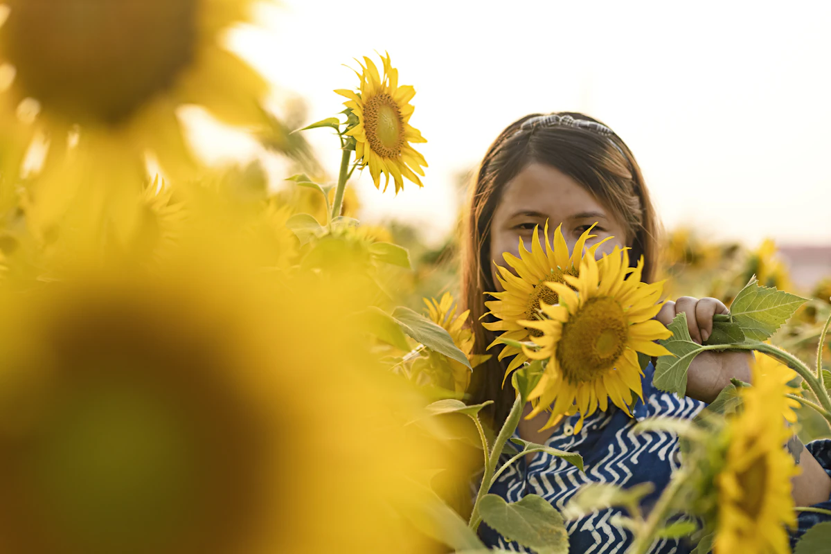 A woman in a blue and white shirt holding a bright yellow sunflower