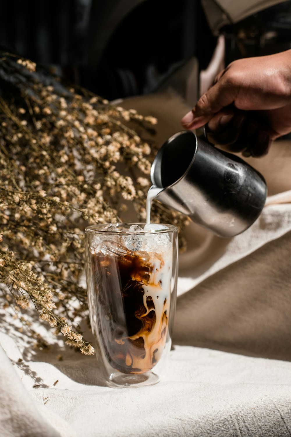 person pouring brown liquid on clear drinking glass