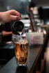person pouring brown liquid on clear drinking glass