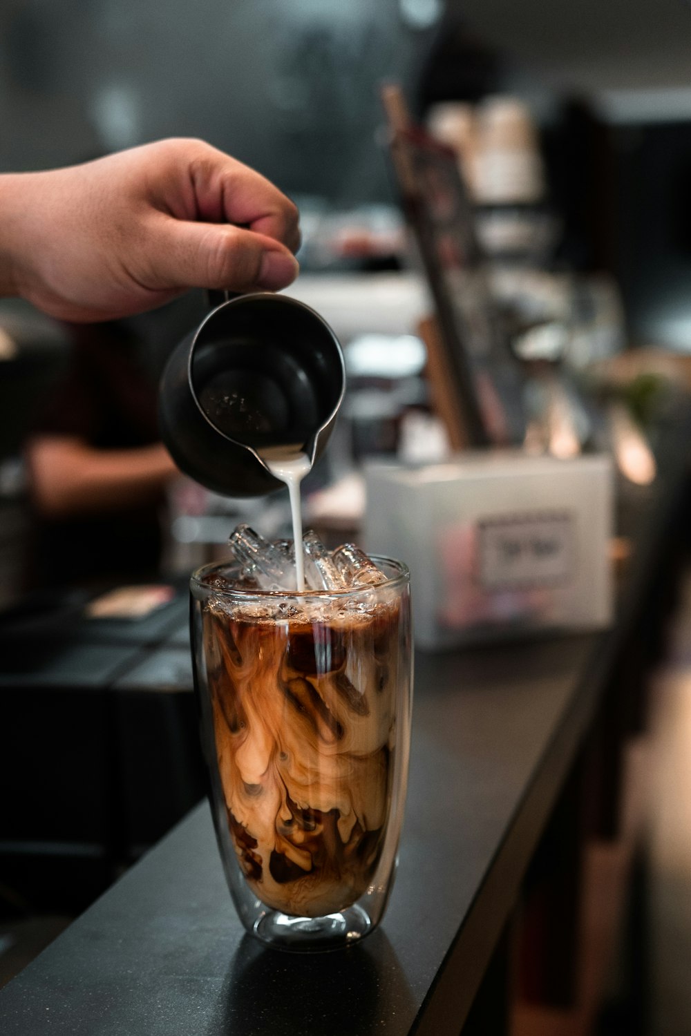 person pouring brown liquid on clear drinking glass