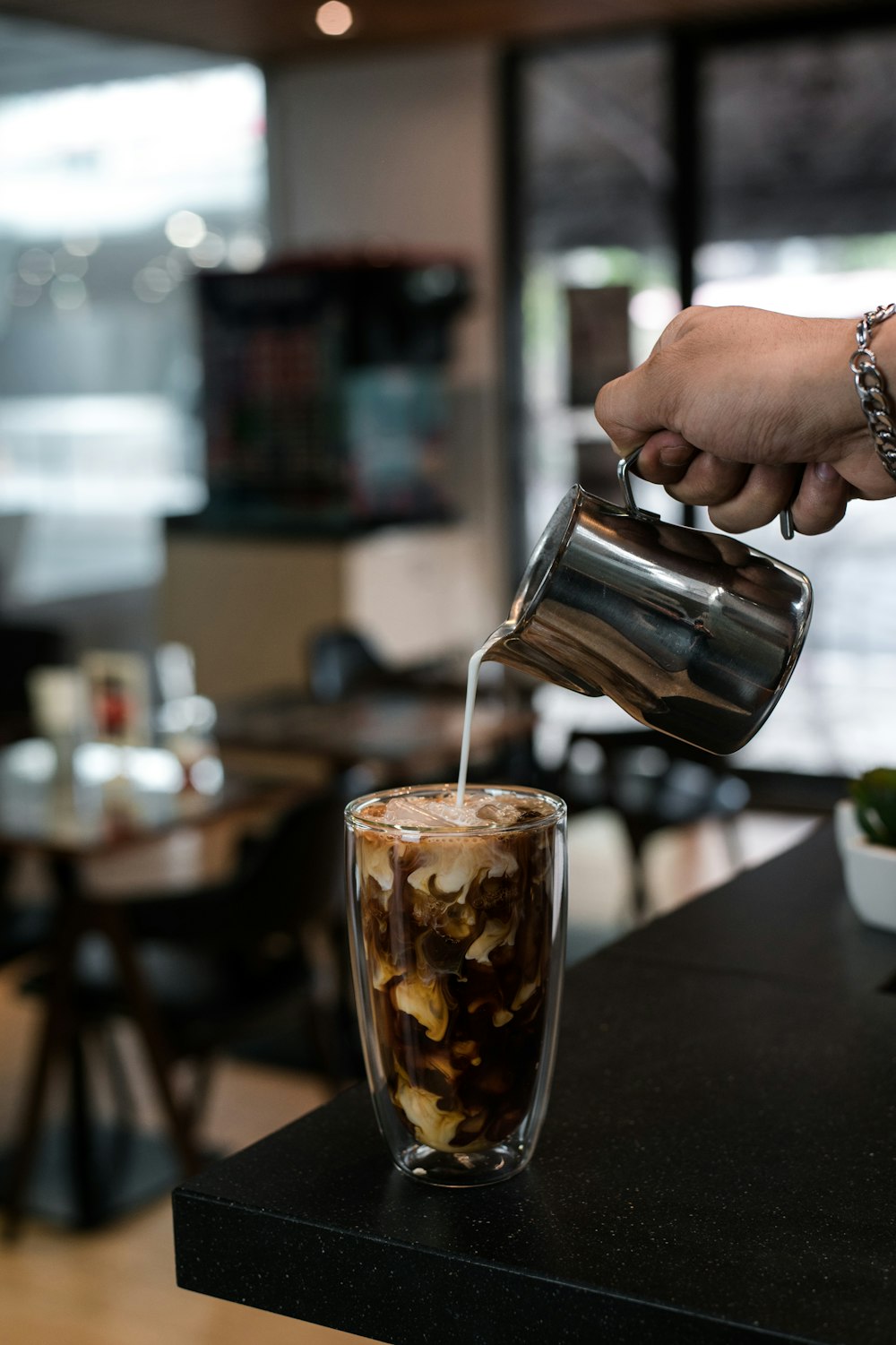 person pouring brown liquid on clear drinking glass