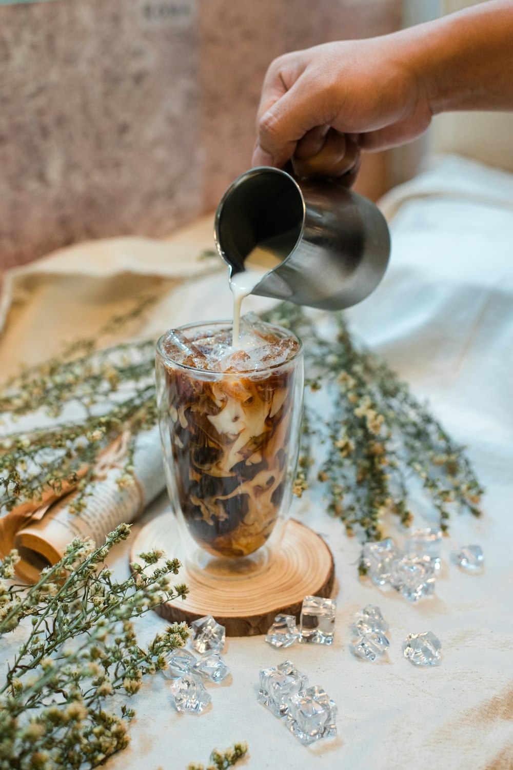 person pouring brown liquid on clear drinking glass