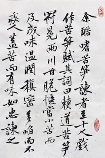 Black ink calligraphy on white paper with characters arranged vertically. There are two red stamps that serve as artistic seals, one in the top right corner and another near the bottom right.