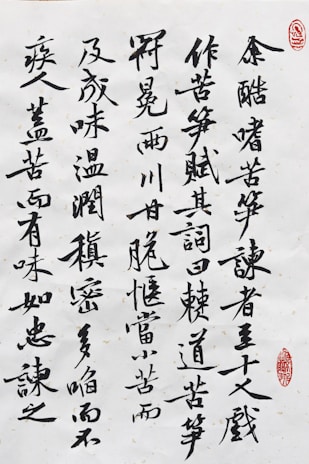 Black ink calligraphy on white paper with characters arranged vertically. There are two red stamps that serve as artistic seals, one in the top right corner and another near the bottom right.
