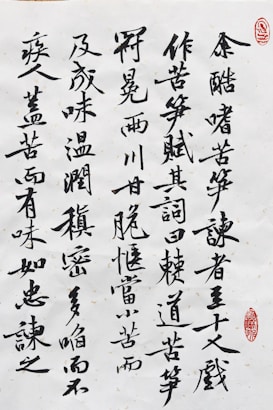 Black ink calligraphy on white paper with characters arranged vertically. There are two red stamps that serve as artistic seals, one in the top right corner and another near the bottom right.