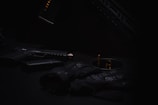 A dark and moody composition features a handgun with a silencer, ammunition, and tactical gloves organized on a surface. The subdued lighting casts shadows, creating a mysterious atmosphere.