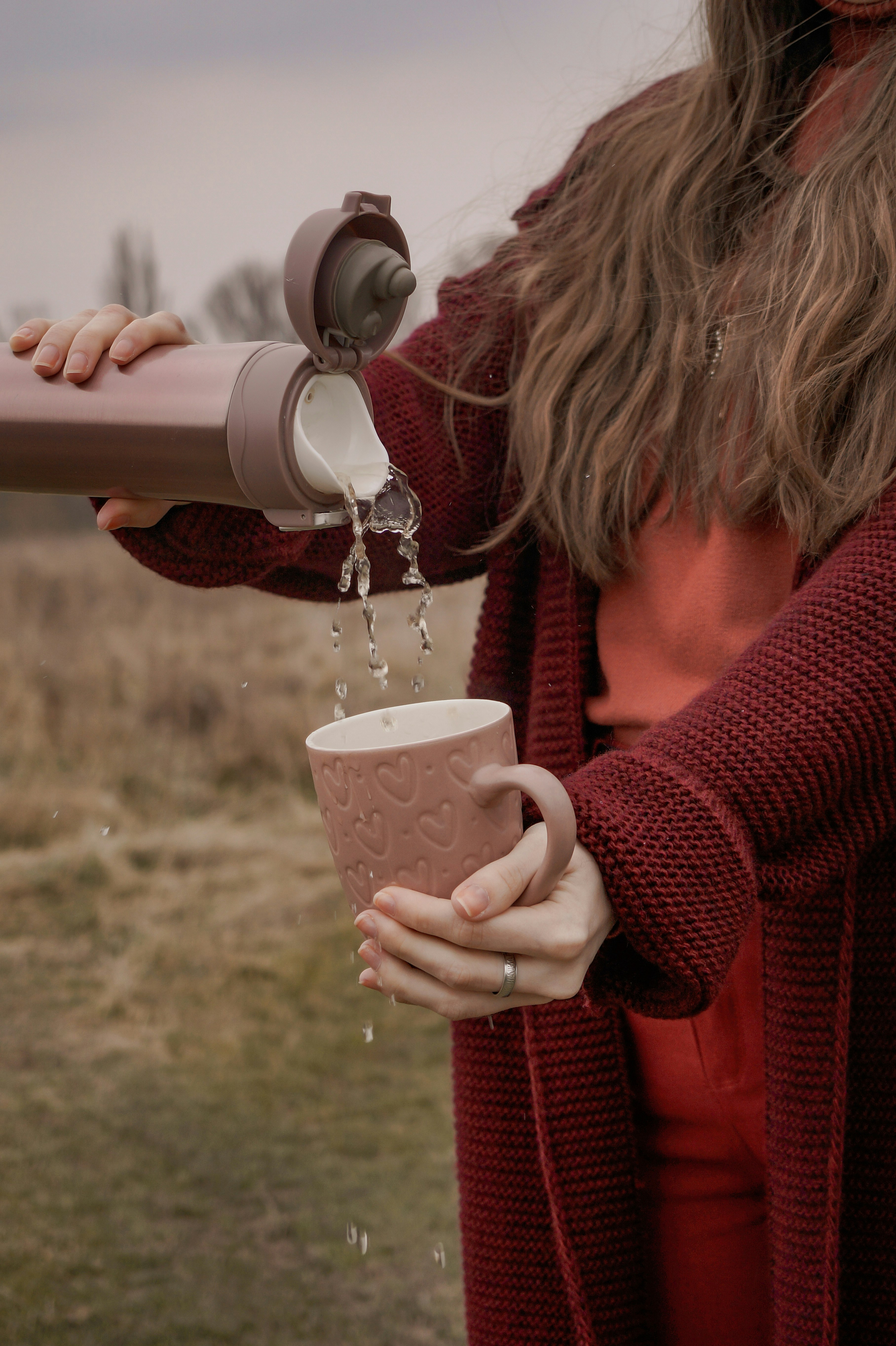 A woman pouring a hot drink from a flask on a country walk