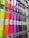 A display rack holding rolls of colorful vinyl wrapped in clear plastic, each roll is labeled and hung on hooks. The colors range from bright neon shades to metallic and glittery finishes.