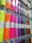 A display rack holding rolls of colorful vinyl wrapped in clear plastic, each roll is labeled and hung on hooks. The colors range from bright neon shades to metallic and glittery finishes.