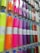 A display rack holding rolls of colorful vinyl wrapped in clear plastic, each roll is labeled and hung on hooks. The colors range from bright neon shades to metallic and glittery finishes.