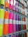 A display rack holding rolls of colorful vinyl wrapped in clear plastic, each roll is labeled and hung on hooks. The colors range from bright neon shades to metallic and glittery finishes.