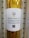 A roll of adhesive glossy vinyl is displayed with a white label featuring a colorful logo at the top. The label contains text in three languages: English, Spanish, and French, describing the product as adhesive glossy vinyl. A QR code is positioned below the text.