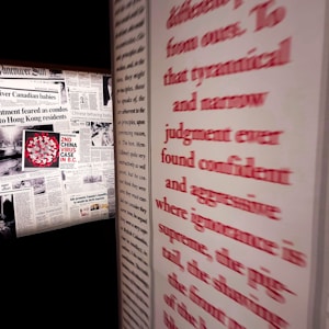A wall featuring multiple newspaper clippings, including headlines related to the 'China virus case' in British Columbia. Prominent red text runs along the right side, partially obscured and emphasizing words like 'tyrannical' and 'aggressive'.