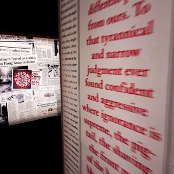 A wall featuring multiple newspaper clippings, including headlines related to the 'China virus case' in British Columbia. Prominent red text runs along the right side, partially obscured and emphasizing words like 'tyrannical' and 'aggressive'.