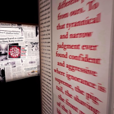 A wall featuring multiple newspaper clippings, including headlines related to the 'China virus case' in British Columbia. Prominent red text runs along the right side, partially obscured and emphasizing words like 'tyrannical' and 'aggressive'.