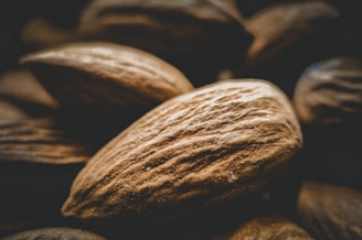 A close-up view of several almonds with a focus on their textured, brown shells. The almonds are clustered together, with lighting highlighting the intricate grooves and natural patterns on the surface.