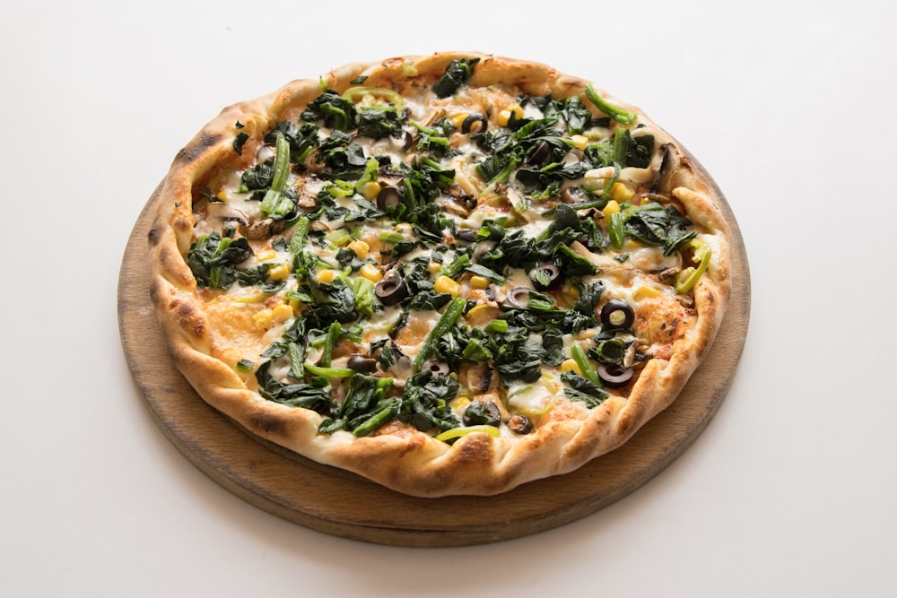 pizza with green leaves and cheese on brown wooden round plate