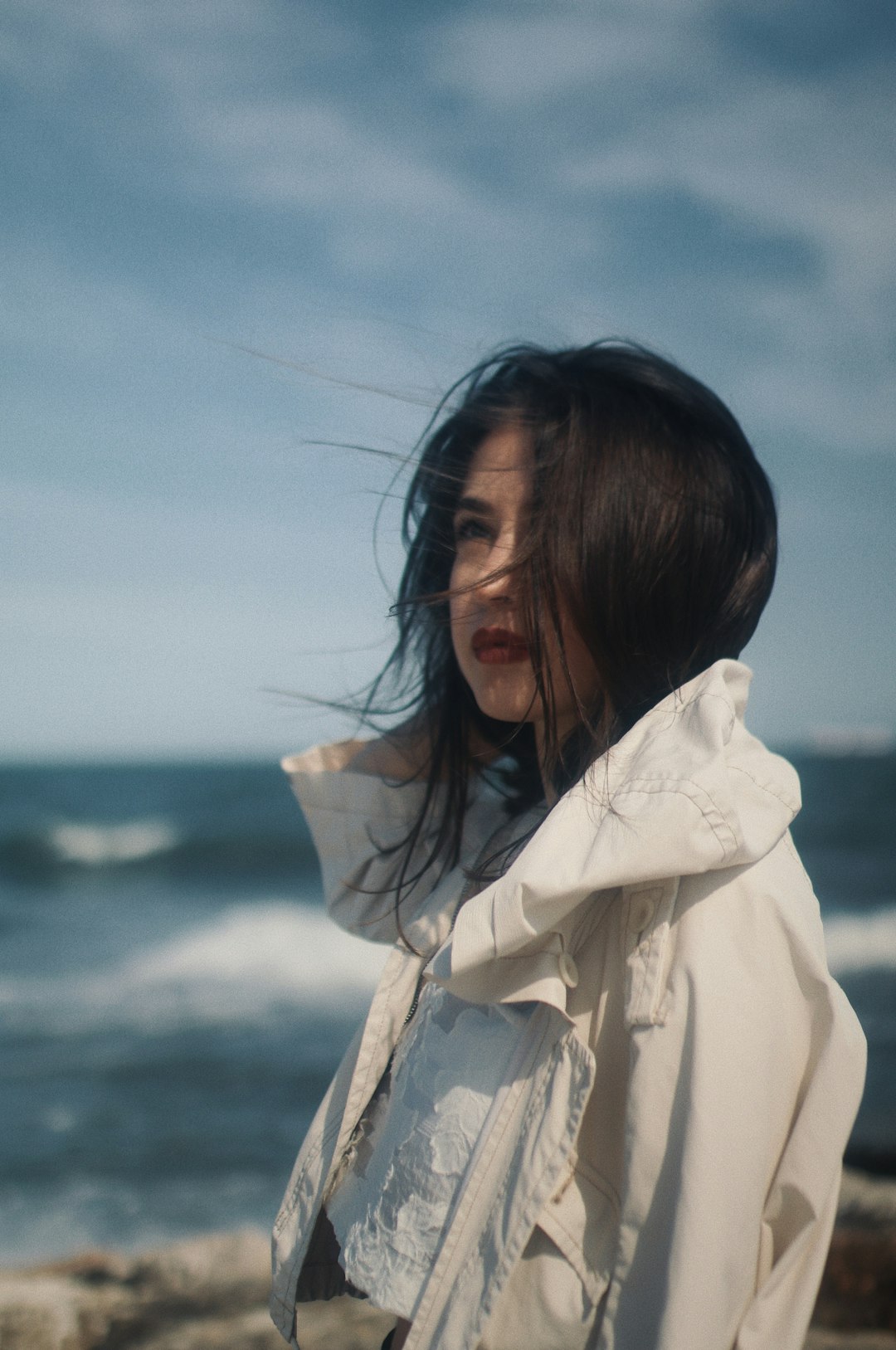 woman in white coat standing near sea during daytime