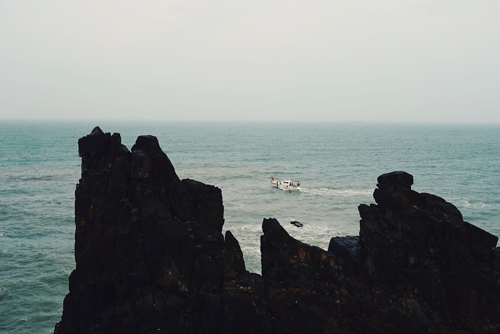 white boat on sea near brown rock formation during daytime