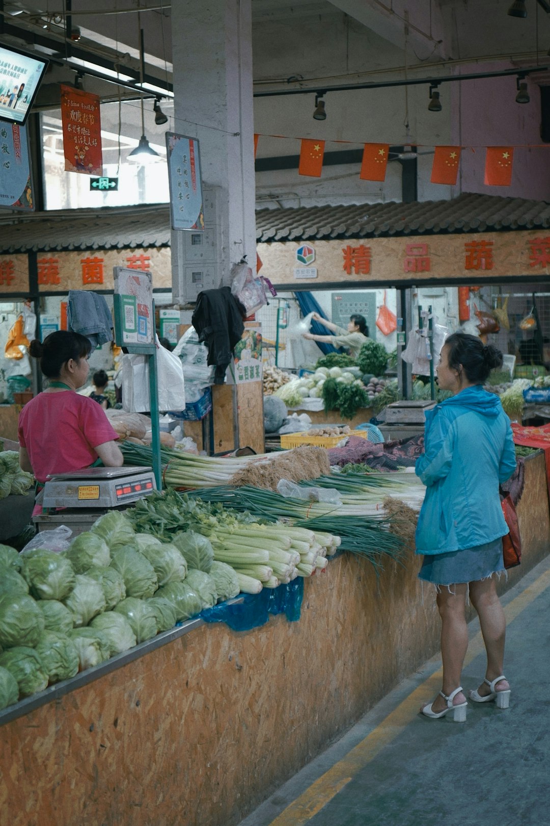 woman in red shirt standing in front of vegetable stand