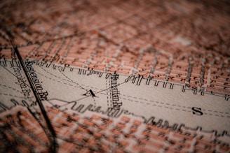 A detailed close-up of a vintage map featuring the Manhattan area. Streets and landmarks are marked in an orange-brown color, with bold black lines denoting paths and boundaries. The texture of the map is visible, providing an aged, tactile quality.