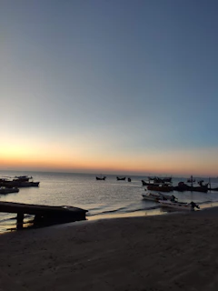 Sunset view over Puerto Escondido beach with colorful boats and a calm ocean horizon.