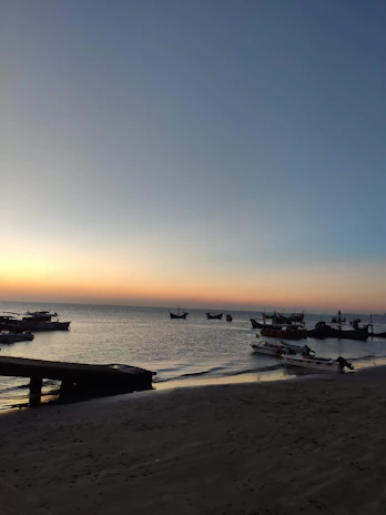Sunset view over Puerto Escondido beach with colorful boats and a calm ocean horizon.