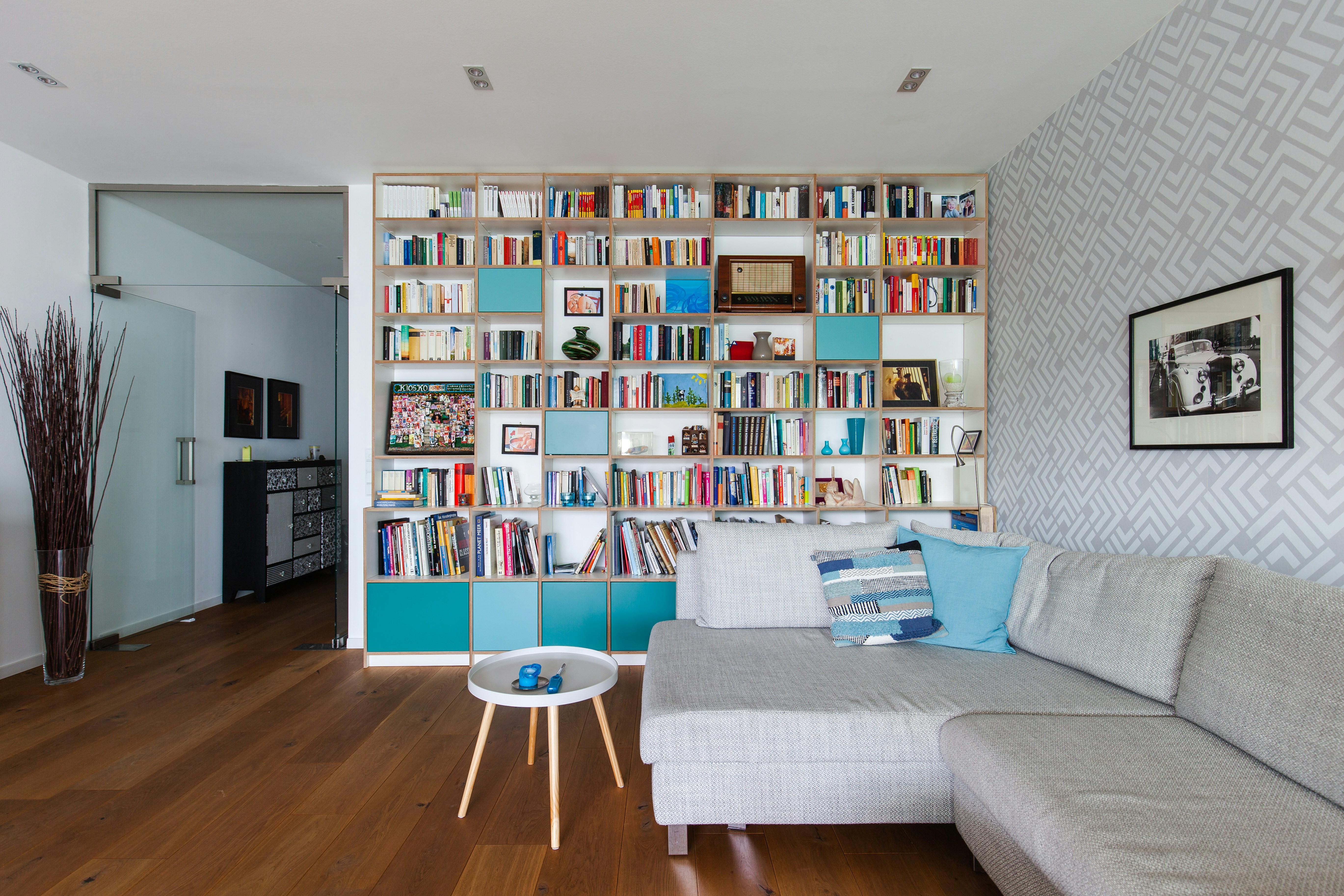Wall-filling bookcase in a large living room. The shelf is made of multiplex with turquoise lacquered doors.