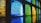 A series of textured glass blocks in various colors, including blue, green, and yellow, arranged in a grid pattern. The glass casts colorful reflections on the surface below, creating a vibrant and dynamic visual effect.
