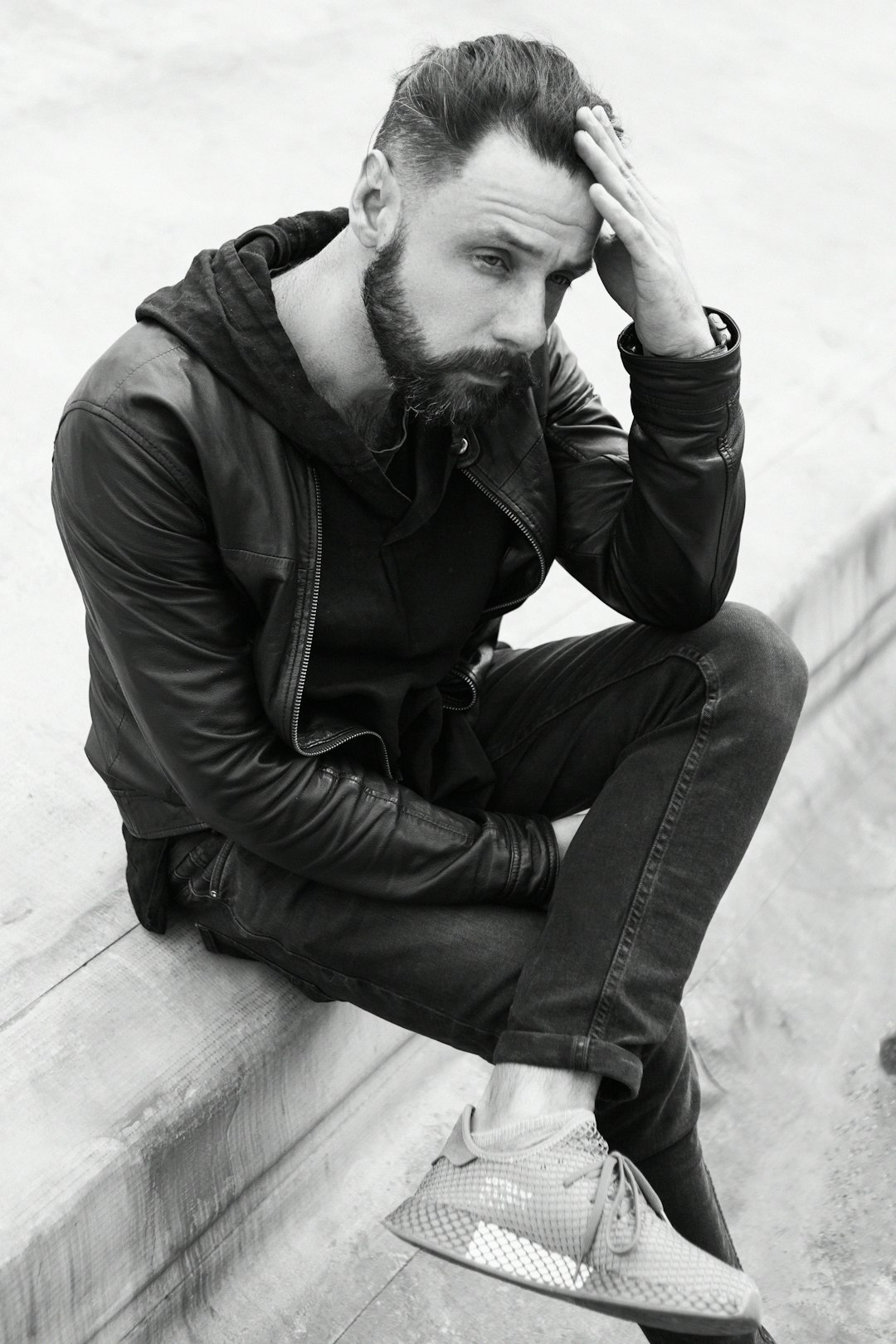 man in black jacket and blue denim jeans sitting on concrete floor