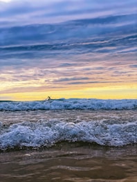 A surfer riding a powerful wave at sunset, with vibrant colors reflecting on the water.