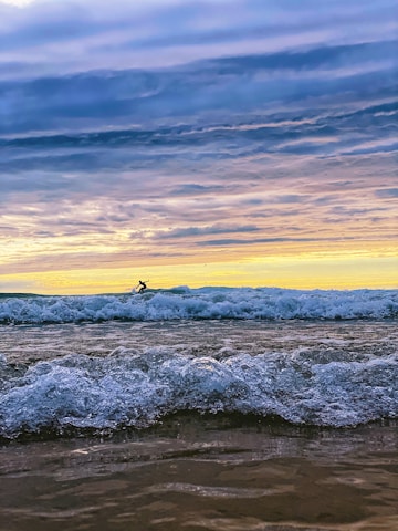 A surfer riding a powerful wave at sunset, with vibrant colors reflecting on the water.