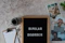 A letter board displays the words 'BIPOLAR DISORDER' surrounded by scattered letters. Nearby, there is a clipboard with a blank sheet of paper and a pencil, accompanied by a cup of black coffee. Three photographs show different facial expressions, and a small potted plant is visible. The surface is textured in a neutral tone.