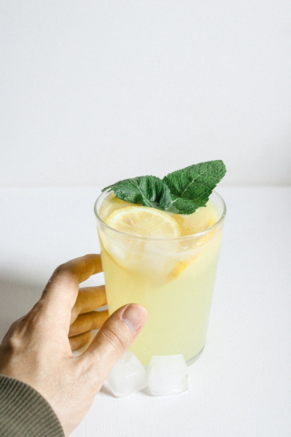 person holding clear drinking glass with yellow liquid